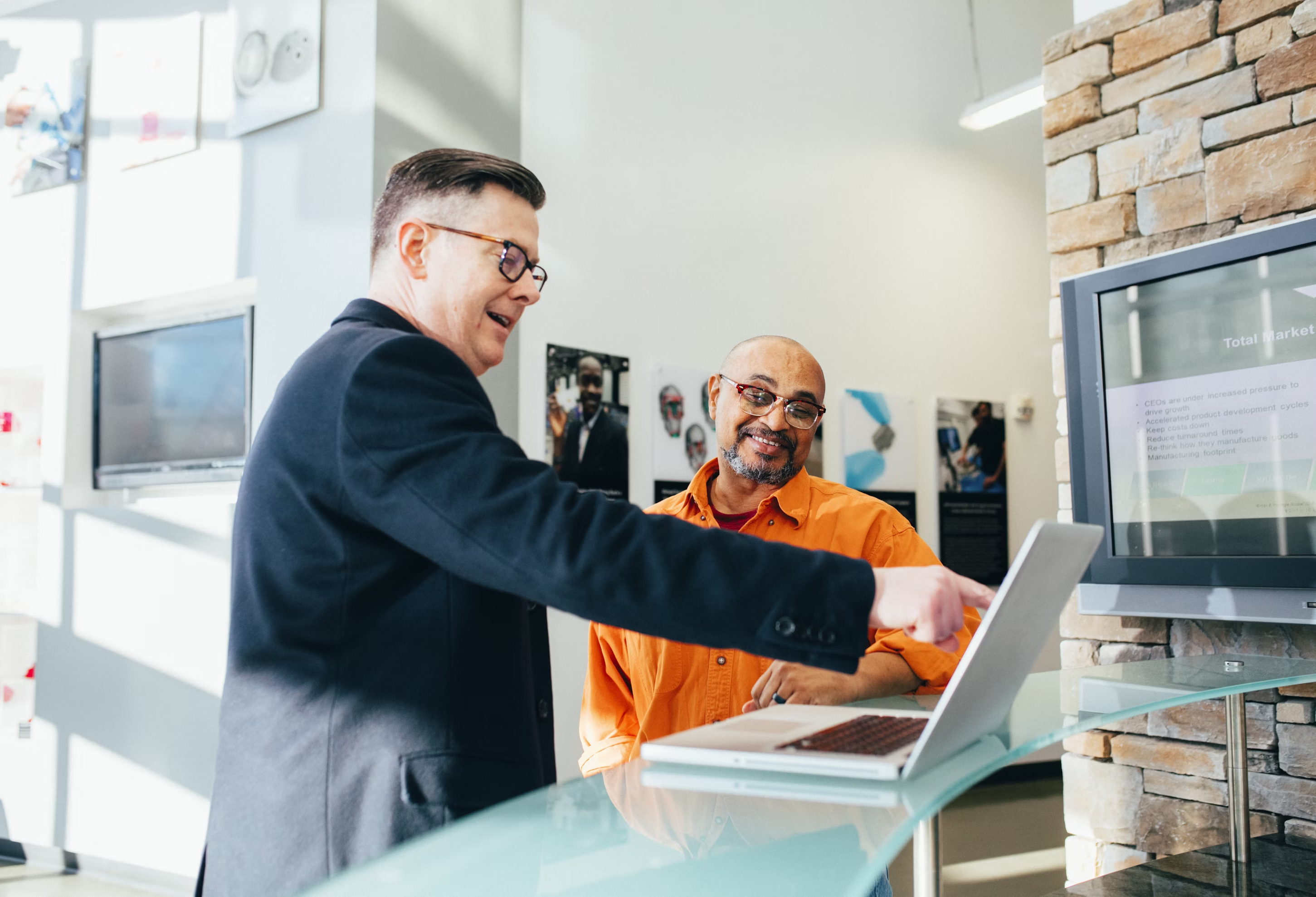 Two men interacting with a laptop in an office setting.