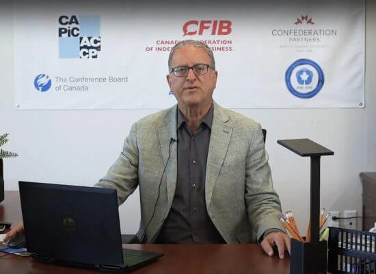 Paul Abraham sitting at a desk with a laptop, in front of a backdrop with multiple logos.