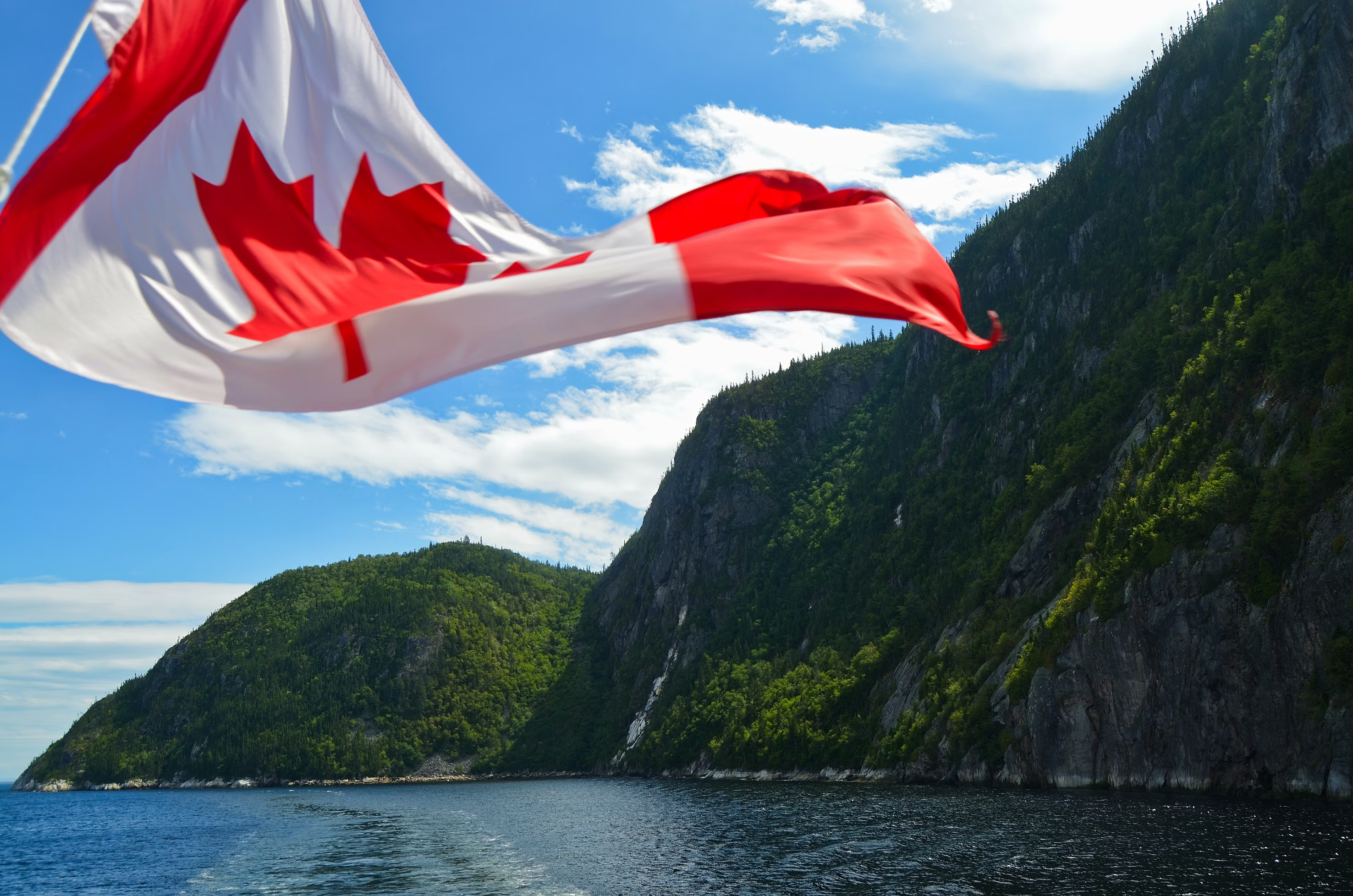 Canadian flag waving in front of a mountainous landscape with water below