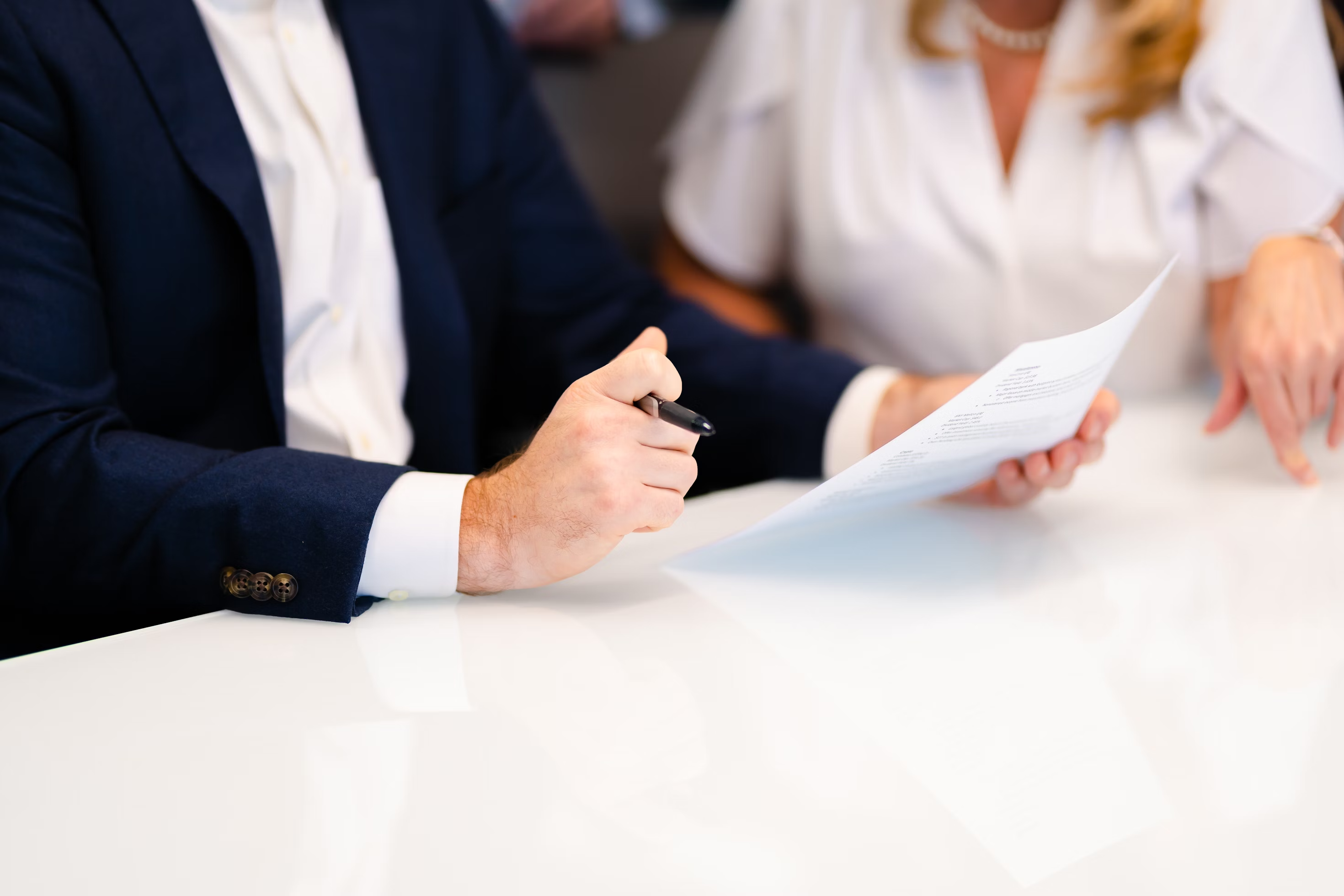 Two people at a table with one holding a pen and looking at a document.